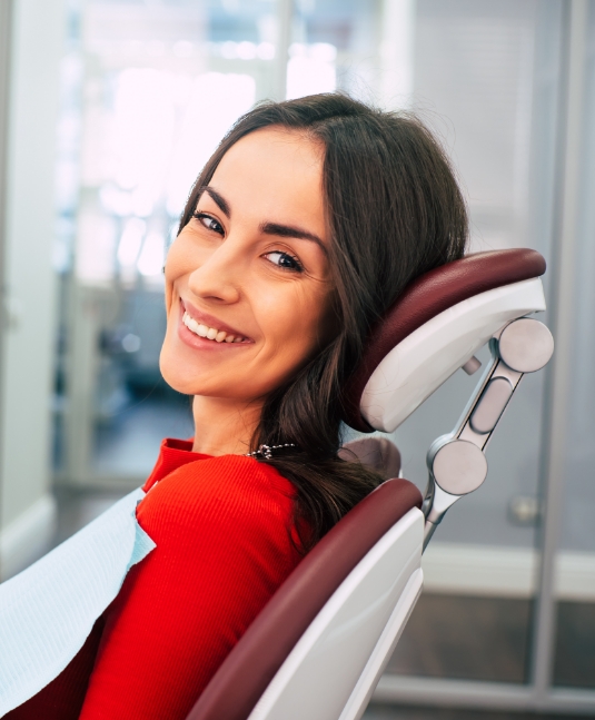 Young woman in red shirt smiling and sitting in dental chair