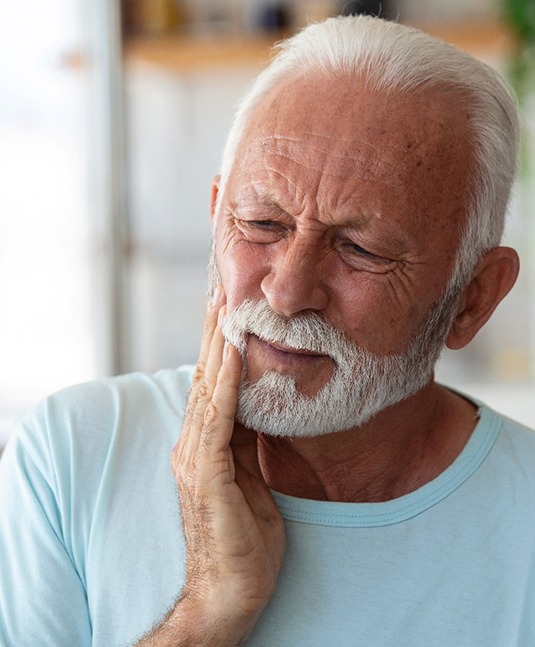 Bearded man on couch rubbing jaw in pain
