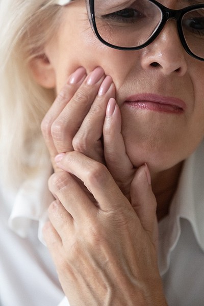 Close-up of senior woman with glasses rubbing her jaw