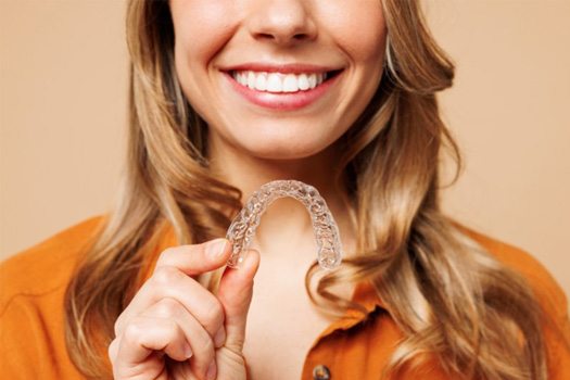 Woman smiling and holding an Invisalign tray