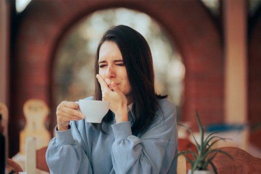 Woman wincing and holding her jaw after taking a sip of coffee