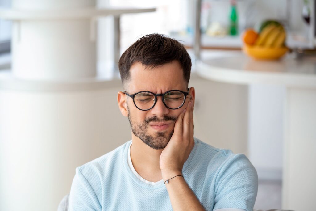 Man in round-framed glasses squinting holding hand to jaw in pain