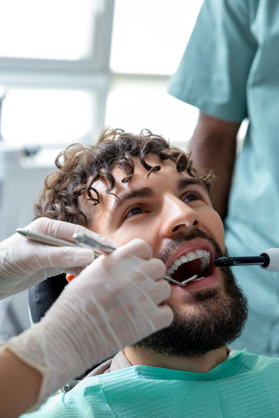 Adult man patient during visit to the clinic for routine cavity checkup sitting in treatment chair receiving orthodontic care