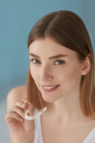 Dental care. Smiling woman with healthy teeth using removable clear braces aligner, orthodontic silicone trainer. Portrait girl with white smile using invisible whitening tray