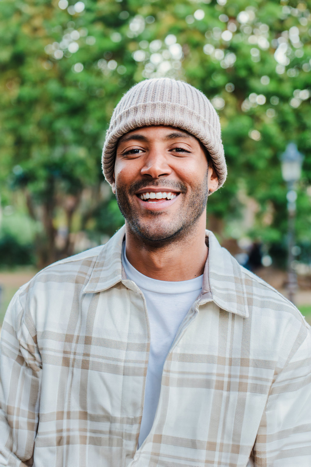 Vertical close up portrait of young hispanic man with a beanie hat smiling and looking at camera outdoors. Front view of latin happy guy standing at park with carefree attitude. Lifestyle concept. High quality photo