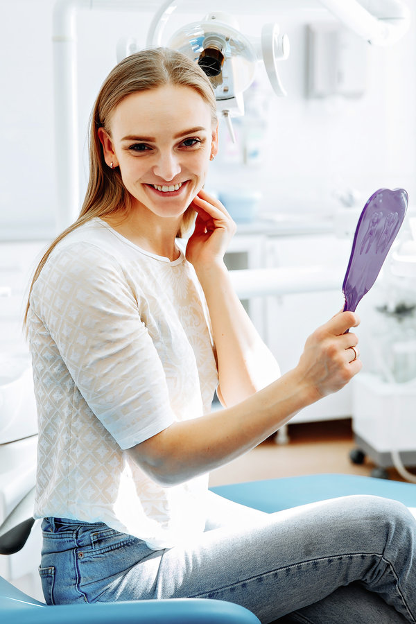 Lady checking teeth in mirror. Young female at dentist office. New dental implants.